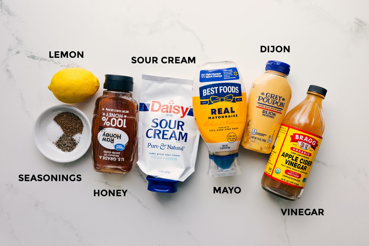 Ingredients In The Dressing For This Easy Coleslaw Dressing Ingredients for the Easy Coleslaw Recipe dressing prepped for easy assembly, including lemon, seasonings, honey, sour cream, mayo, Dijon, and vinegar.