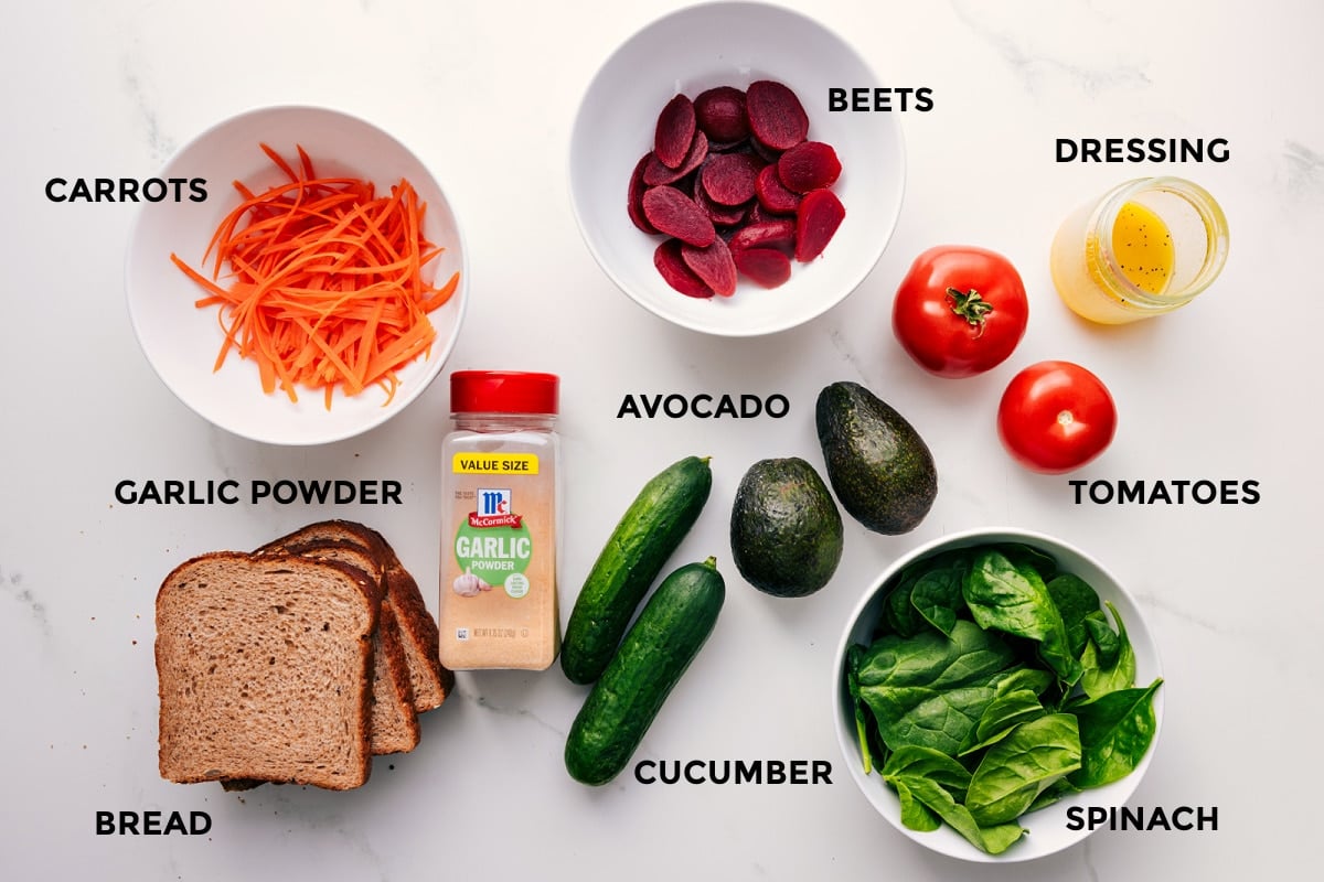 Ingredients In This Veggie Sandwich All the ingredients in this recipe prepped out for easy assembly including the carrots, garlic powder, bread, beets, avocado, cucumber, spinach, tomatoes, and dressing.