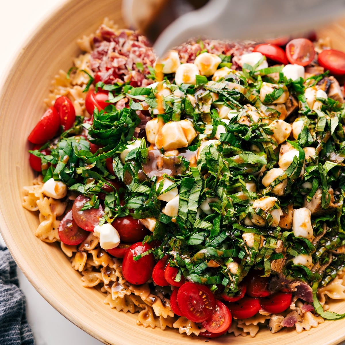 How To Make This Caprese Pasta Salad Dressing being poured over Caprese Pasta Salad in a large bowl before being tossed together.