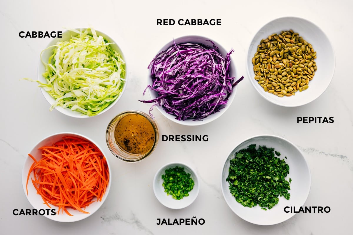 Ingredients In This Healthy Slaw Ingredients prepped for easy assembly, including green and red cabbage, carrots, jalapeño, cilantro, pepitas, and dressing.
