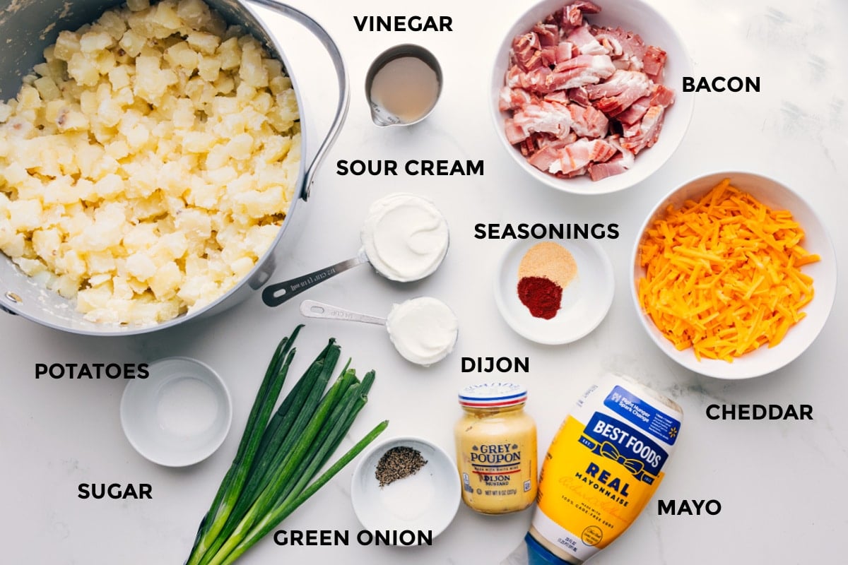 Ingredients In This Loaded Potato Salad All the ingredients in this recipe prepped out for easy assembly including the potatoes, sugar, green onions, mayo, cheddar, seasonings, sour cream, vinegar, and bacon.