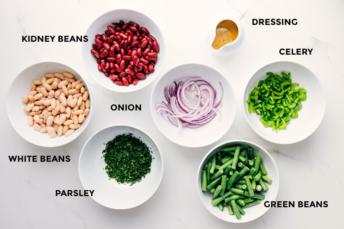Ingredients In This Three Bean Salad All the ingredients in this recipe prepped out for easy assembly including the beans, parsley, onion, green beans, celery, and dressing.