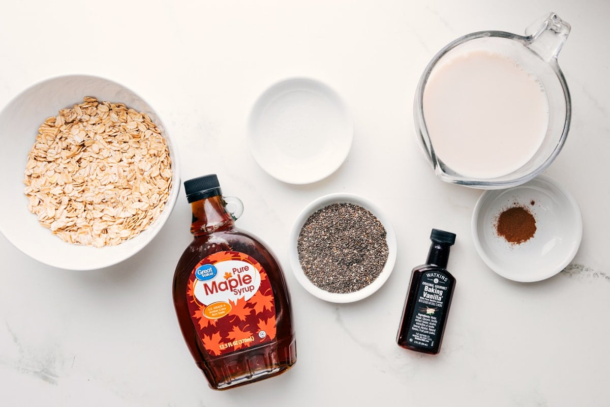 All the ingredients in this recipe prepped out for easy assembly including the oats, mape syrup, milk, cinnamon, chia seeds, vanilla, an salt.