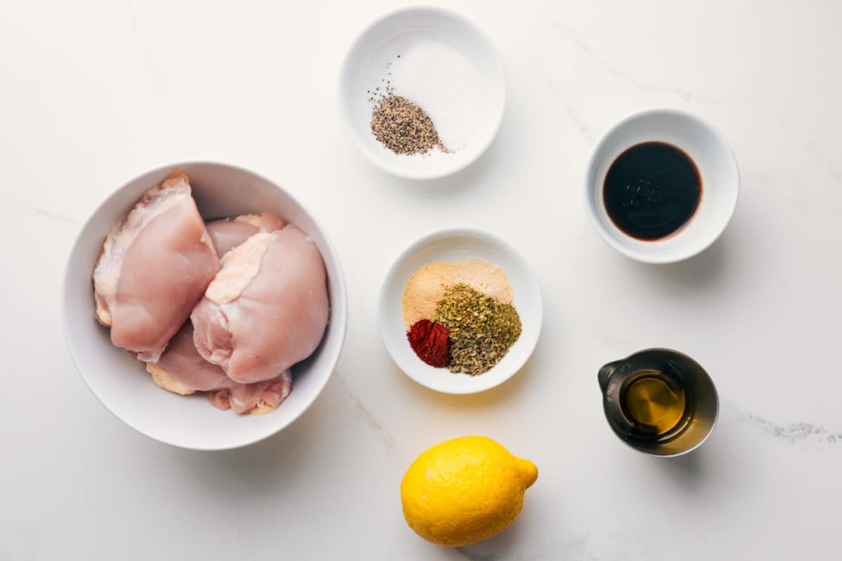 All the ingredients in this recipe prepped out for easy assembly including the chicken, seasonings, balsamic vinegar, olive oil, and lemon.