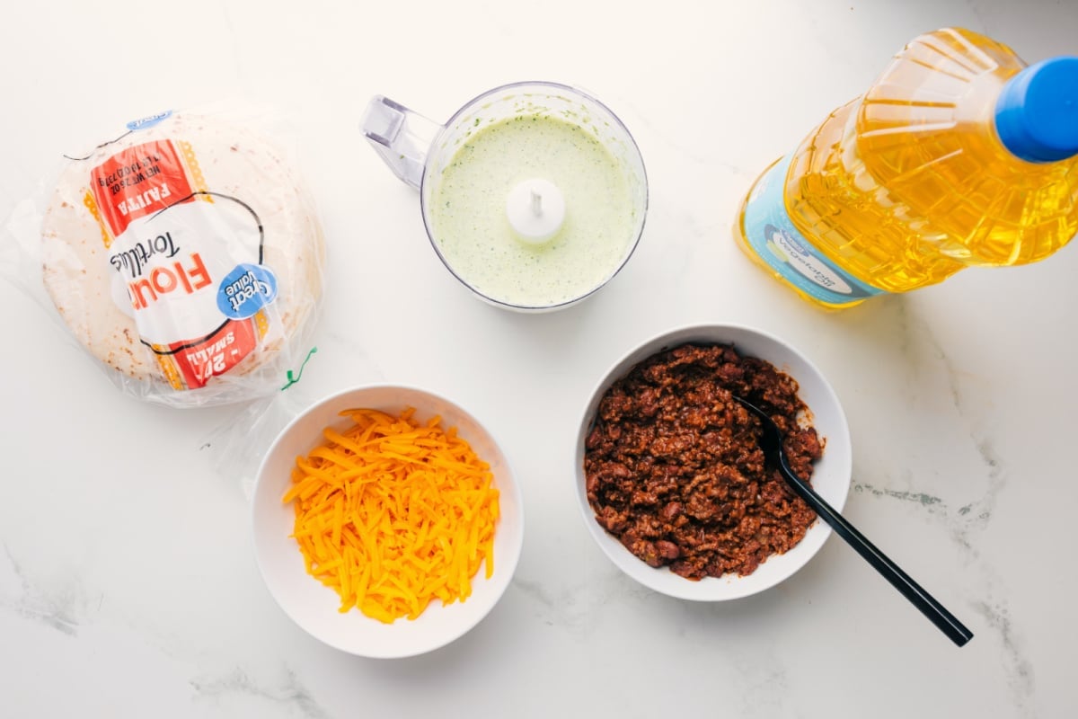 All the ingredients in this recipe prepped out for easy assembly including the tortillas, cheese, sauce, beef, and oil.