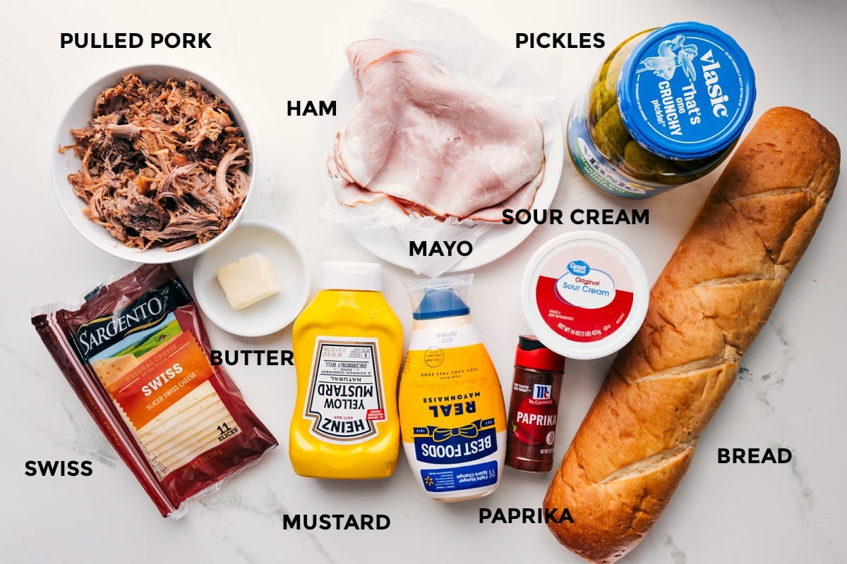 Ingredients In Cuban Sandwich Recipe Ingredients in this recipe prepped out for easy assembly including the pulled pork, swiss, butter, ham, mustard, paprika, sour cream, bread, and pickles.