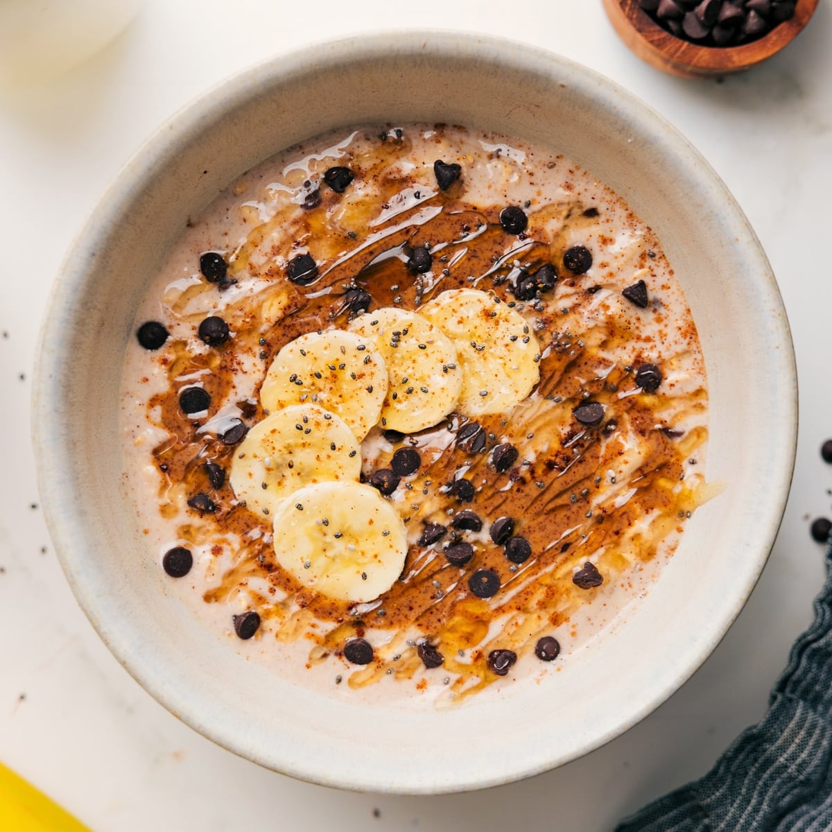 Banana Overnight Oats Recipes topped with peanut butter, sliced bananas, chocolate chips, and honey.