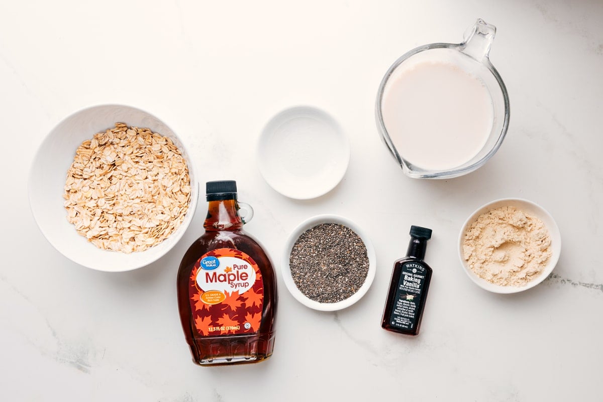 All the ingredients in this recipe prepped out for easy assembly including the oats, maple syrup, chia seeds, milk, protein powder, vanilla, and salt.