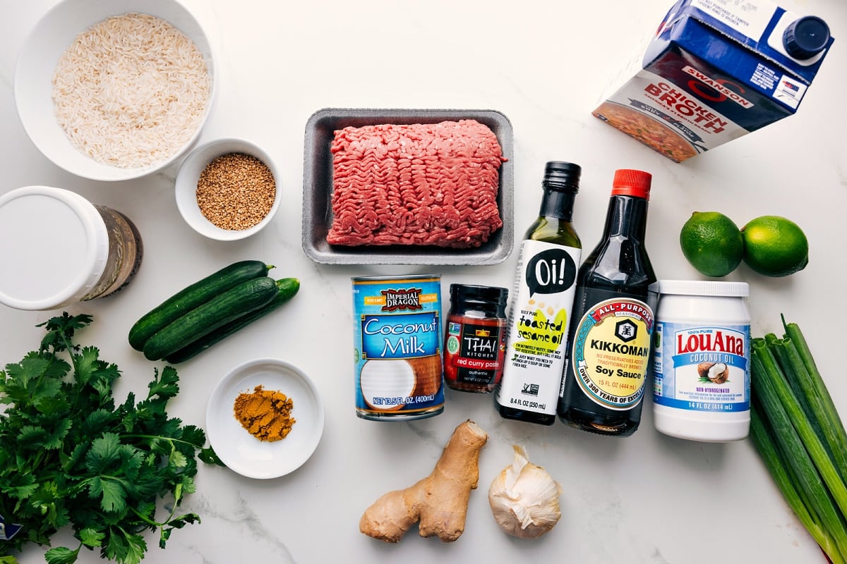 All the ingredients in this recipe prepped out for easy assembly including the rice, sesame seeds, cilantro, cucumbers, coconut milk, red curry paste, toasted sesame oil, soy sauce, coconut oil, ginger, garlic, green onions, limes, and broth.