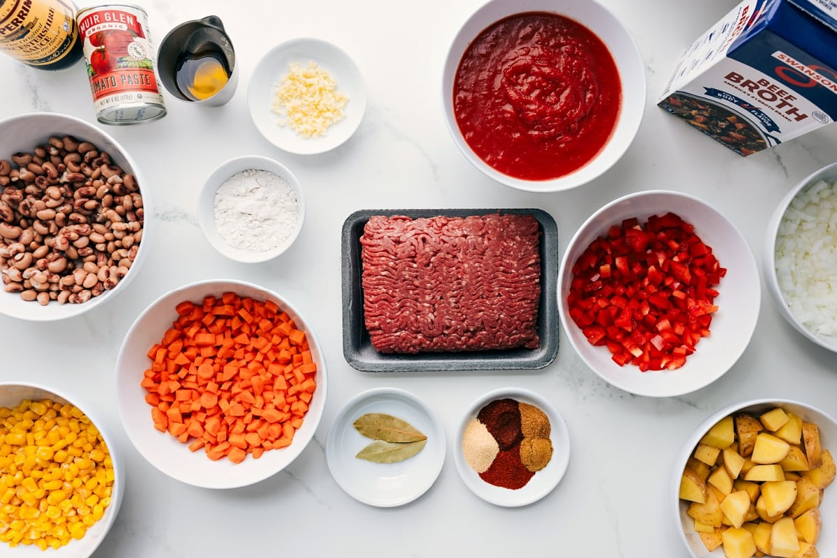 All the ingredients prepped for this recipe, including tomato paste, Worcestershire sauce, black-eyed peas, corn, potatoes, beef broth, bouillon, veggies, seasonings, and ground beef.