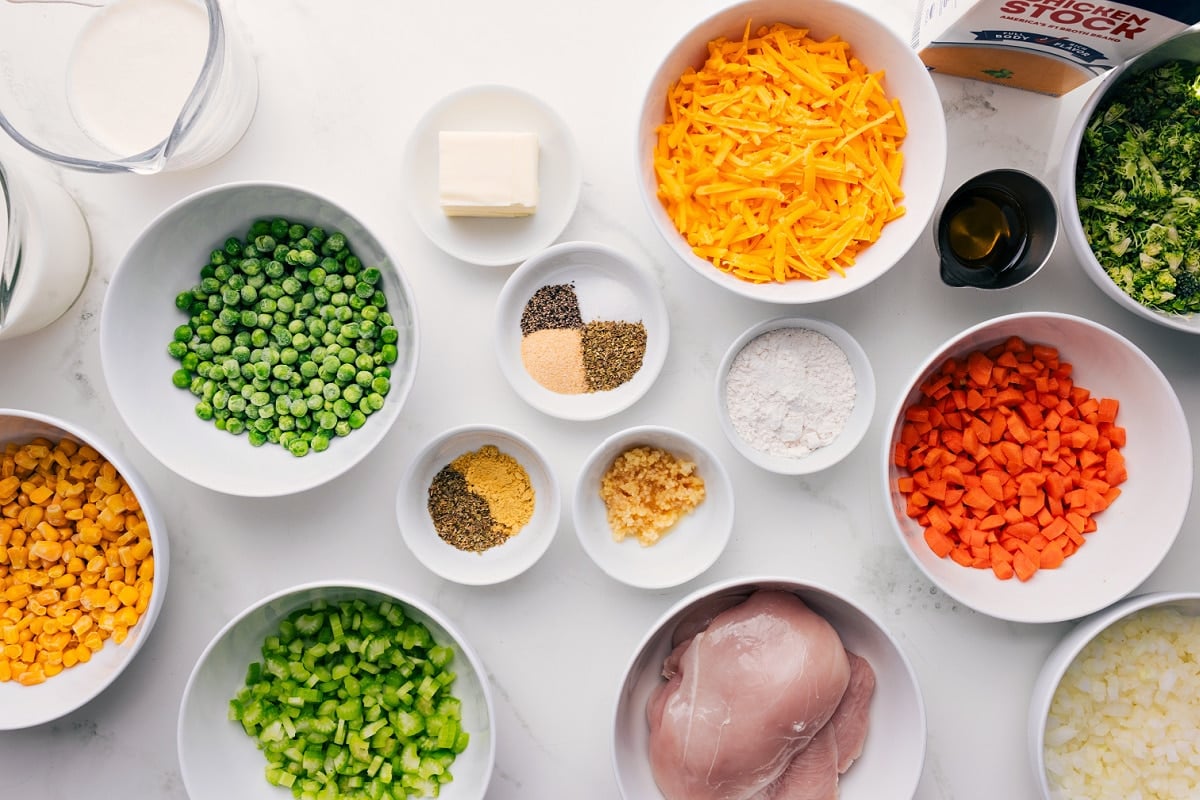 All the ingredients in this recipe prepped out for easy assembly including the milk, peas, corn, celery, seasonings, butter, chicken, cheese, carrots, onions, broccoli, oil, and stock.