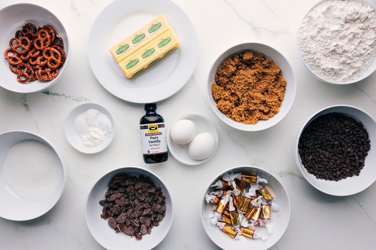 All the ingredients in this recipe prepped out for easy assembly including the pretzels, butter, sugar, baking agents, chocolate, caramels, brown sugar, and flour.