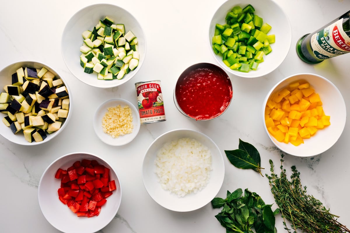All the ingredients in this recipe prepped out for easy assembly including the veggies, tomatoes, oil, garlic, tomato paste, and fresh herbs.