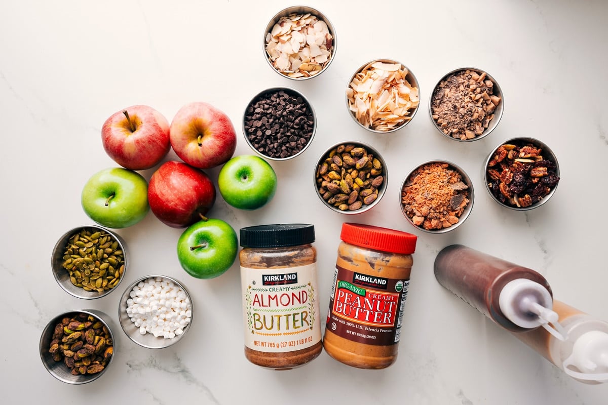 All the ingredients in this recipe prepped out for easy assembly including apples, pepitas, marshmallows, nuts, granola, chocolate, toffee bits, butterfingers, almond butter, peanut butter, chocolate, and caramel.