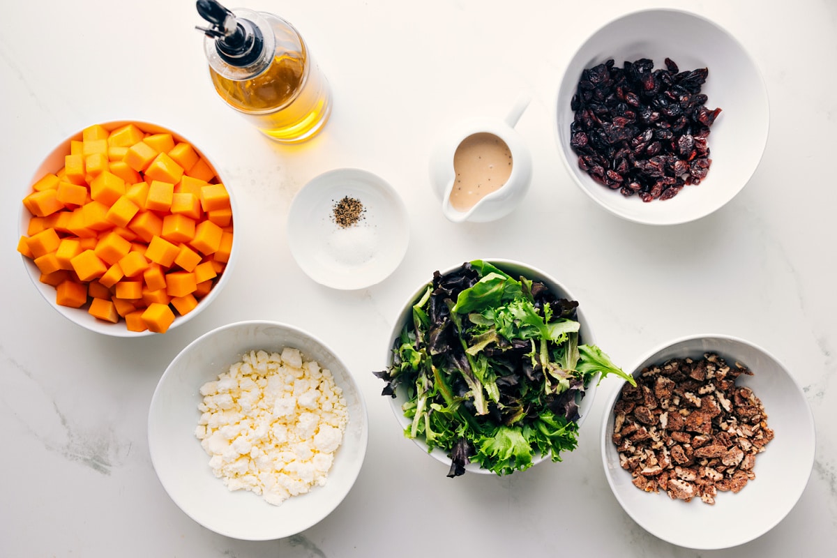 Butternut Squash Salad All the ingredients in this recipe prepped out for easy assembly including the sweet potatoes, feta, mixed greens, nuts, dried cranberries, dressing, seasonings, and oil.