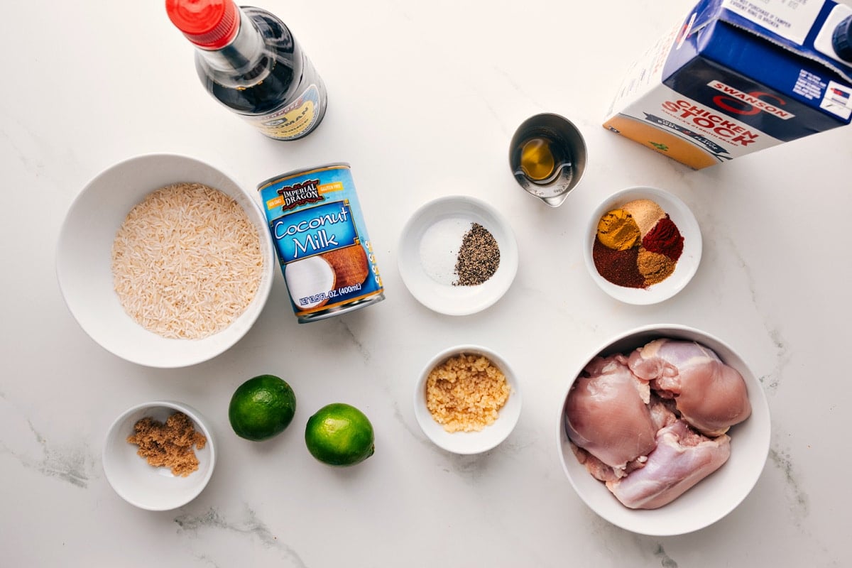 All the ingredients in this recipe prepped out for easy assembly including the rice, coconut milk, garlic, ginger, seasonings, stock, soy sauce, and limes.