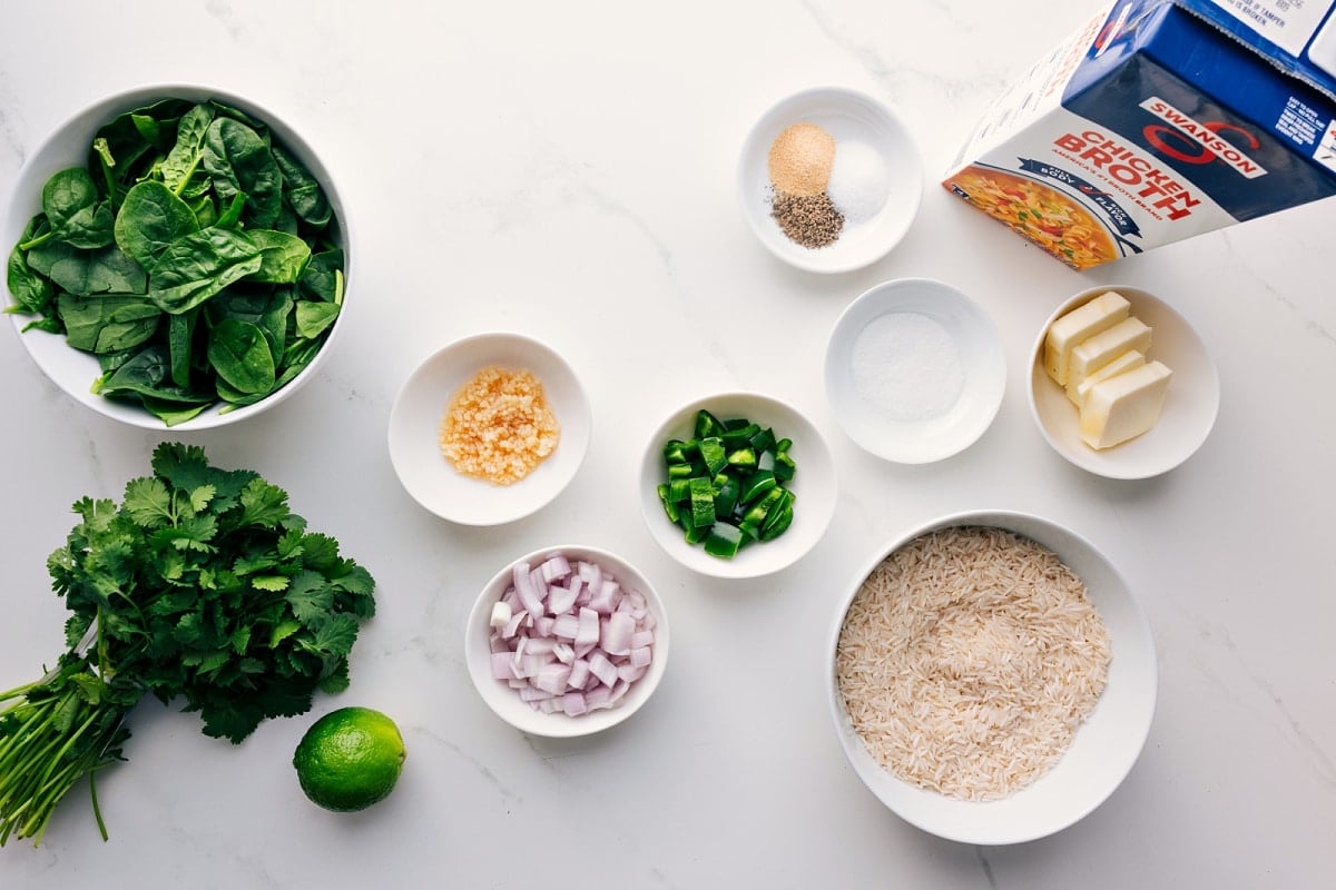 All the ingredients in this recipe including the spinach, cilantro, lime, garlic, shallots, jalapeño, rice, sugar, seasonings, butter, and broth.