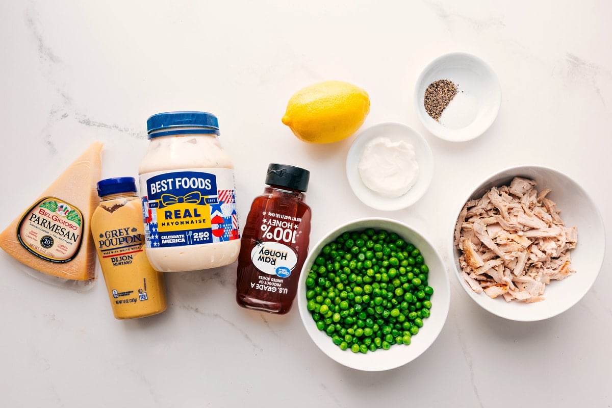 All the ingredients in this recipe prepped out for easy assembly including the parmesan, dijon, mayo, honey, peas, lemon, salt, pepper, chicken, and sour cream.